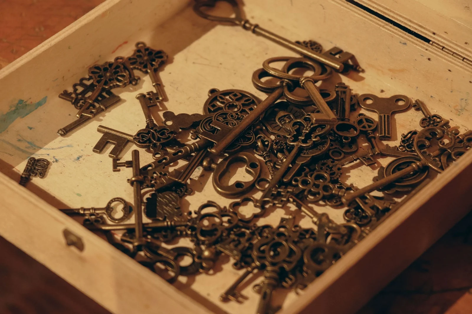 A shallow wooden box filled with several dozen mismatched antique keys of different shapes and sizes.