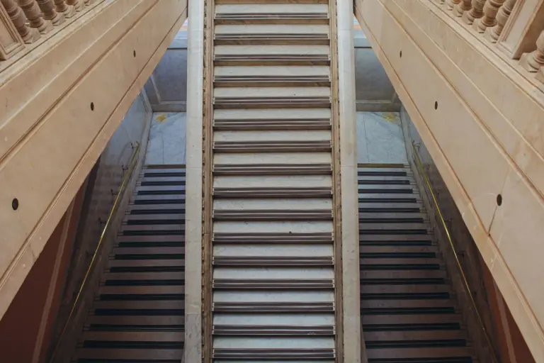 Two parallel flights of stone stairs rising side by side, separated by a central wall, inside a pale stone building.