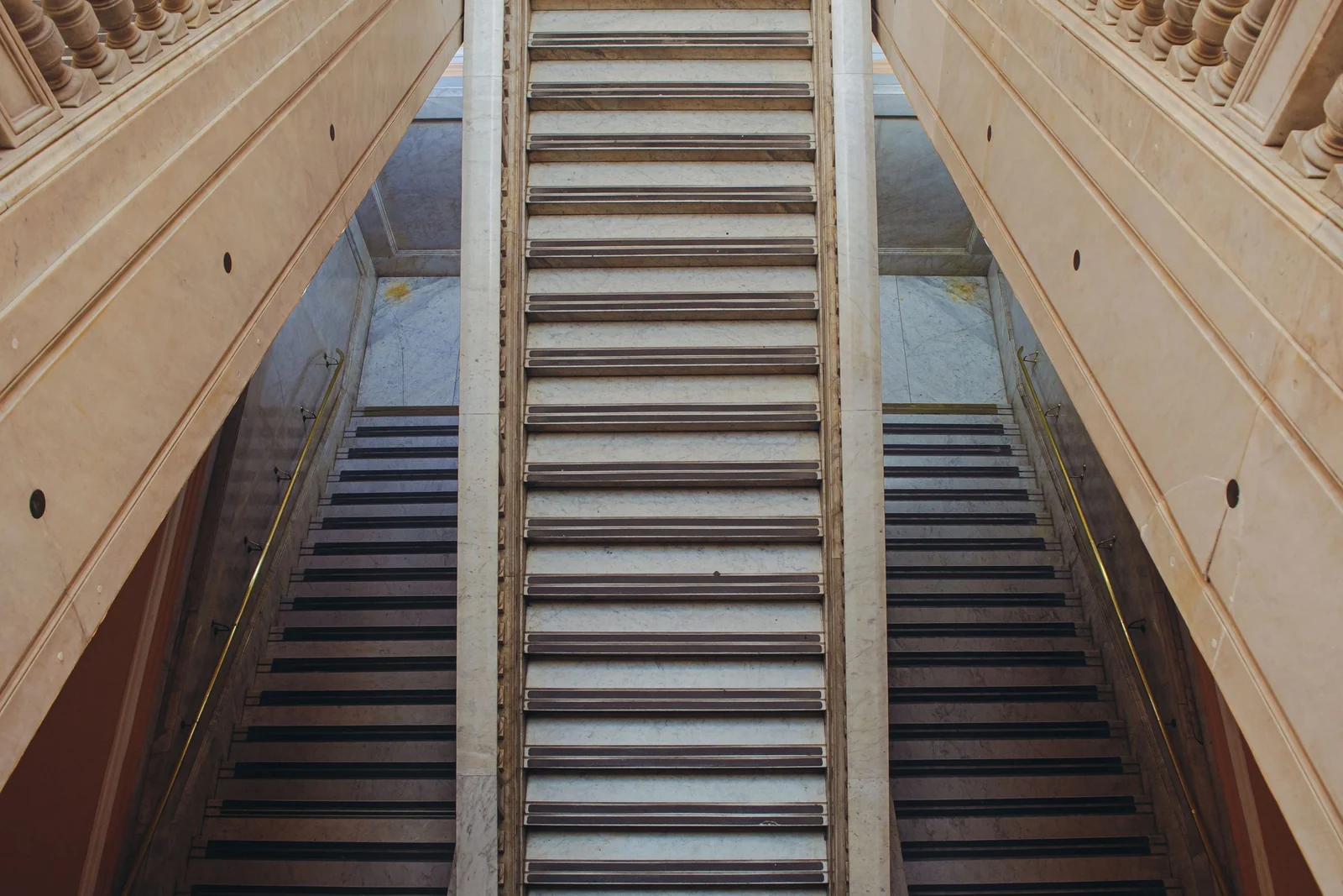Two parallel flights of stone stairs rising side by side, separated by a central wall, inside a pale stone building.