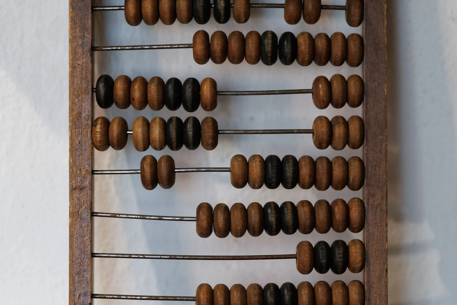 A close view of a wooden abacus with rows of dark and light beads threaded on metal rods.