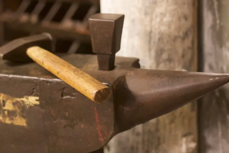 A blacksmith's anvil with a hammer resting across it in a workshop.