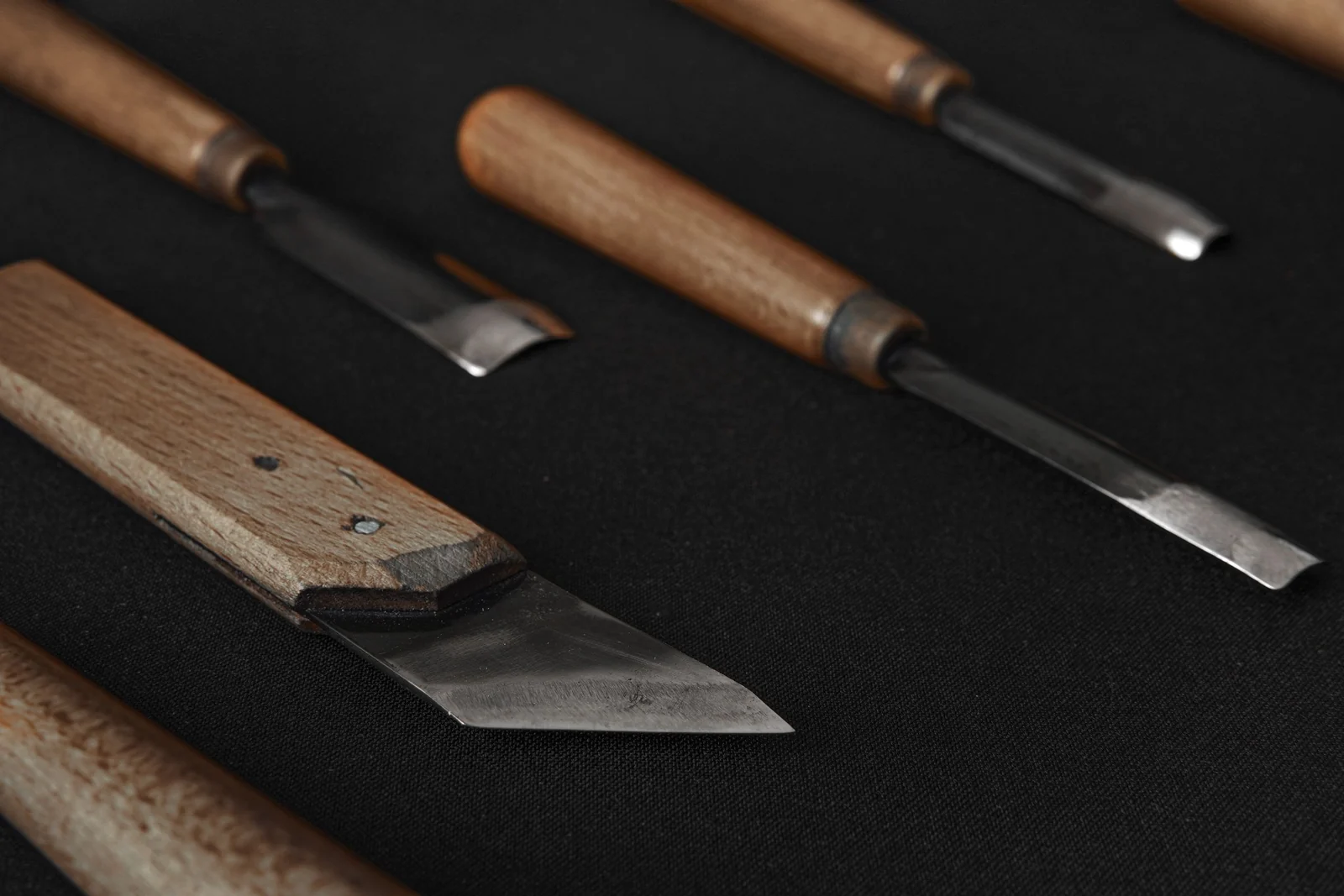 Woodcarving chisels and a marking knife with wooden handles on a black surface.