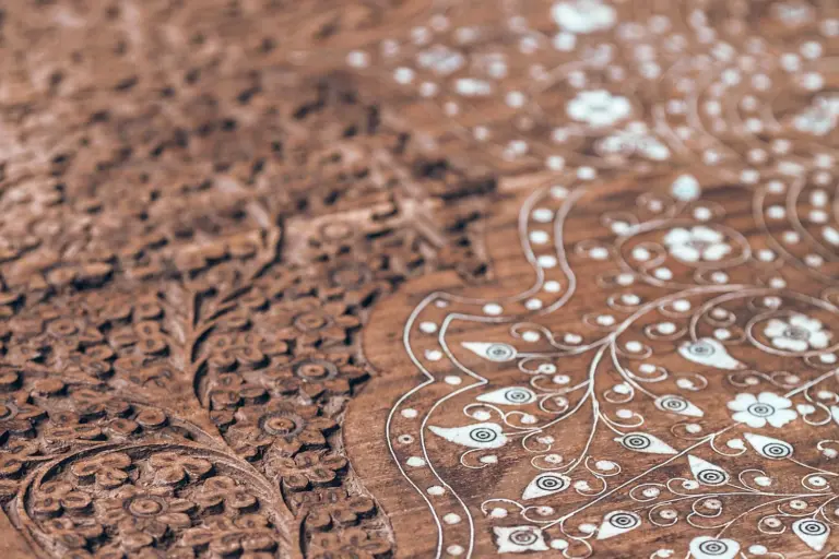 A close-up of a hand-carved wooden surface where dense chiselled ornament fades into soft focus.