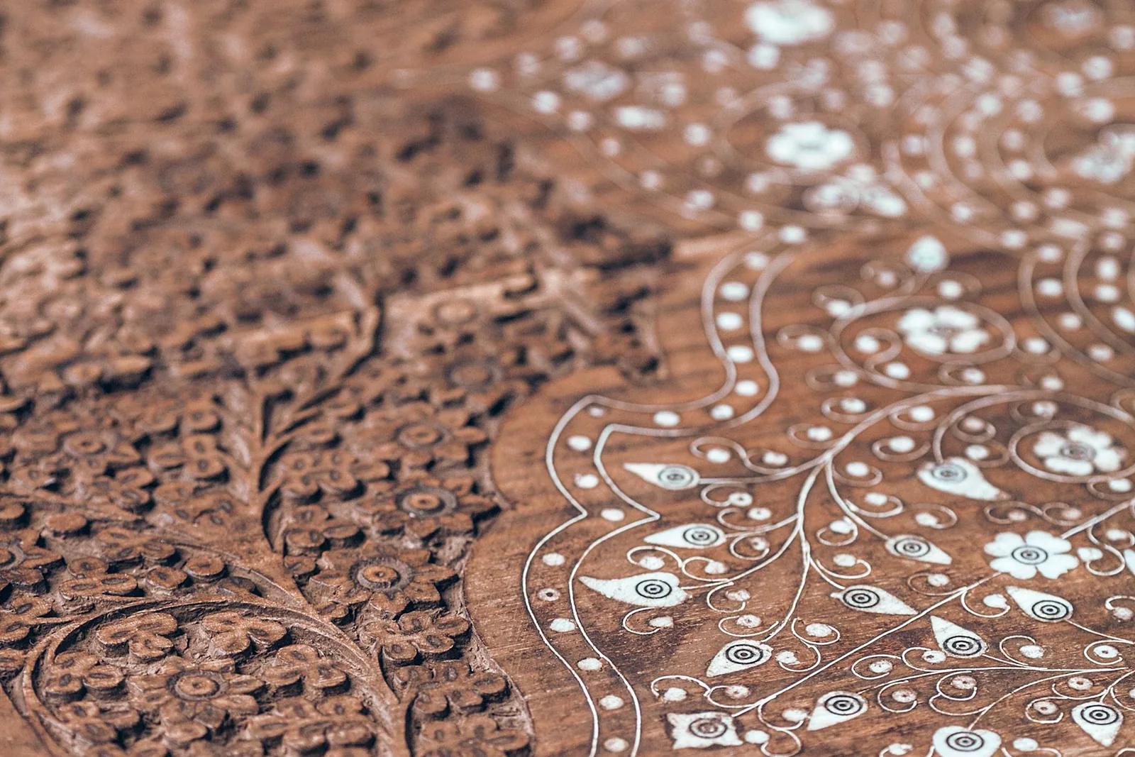 A close-up of a hand-carved wooden surface where dense chiselled ornament fades into soft focus.