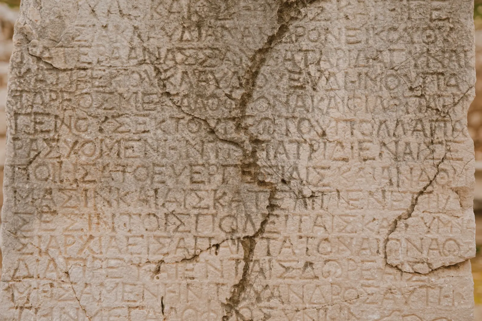 Rows of ancient Greek letters are incised into the face of a weathered, cracked sandstone slab.