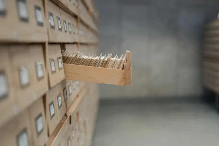 A wooden library card index with one drawer pulled open, full of filing cards.