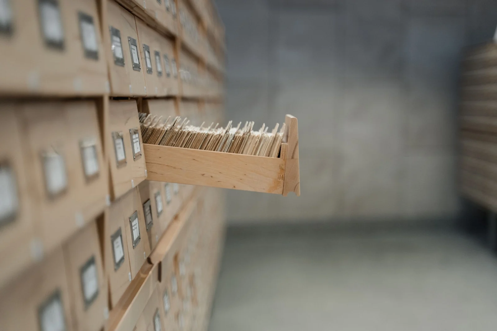 A wooden library card index with one drawer pulled open, full of filing cards.