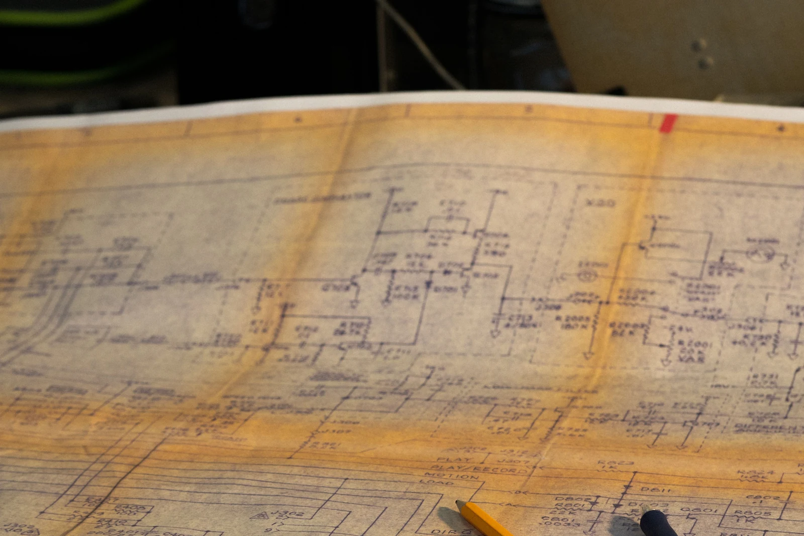 An aged ochre engineering drawing covered in ruled lines and hand-lettered annotations lies open on a desk.