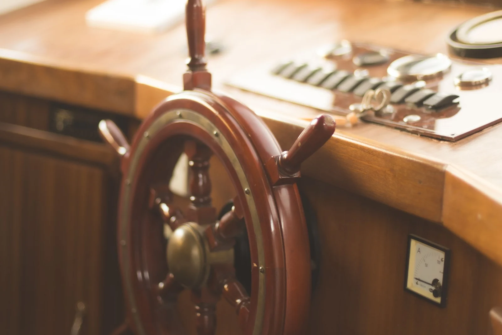 A wooden ship's wheel with a brass hub beside a boat's control console.