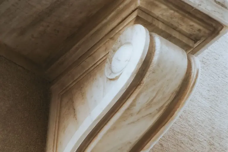 A carved stone corbel projects from a wall and carries the weight of the moulded cornice resting on it.