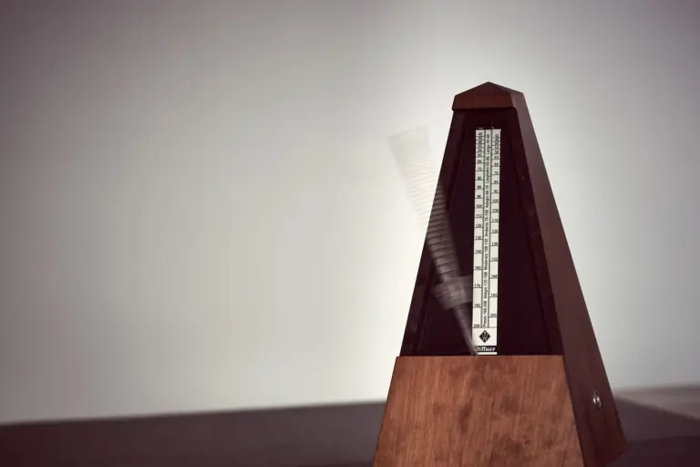 A wooden metronome seen close up, its weighted arm blurred as it swings from one side to the other.