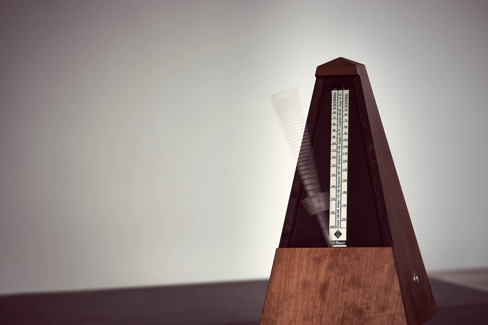 A wooden metronome seen close up, its weighted arm blurred as it swings from one side to the other.