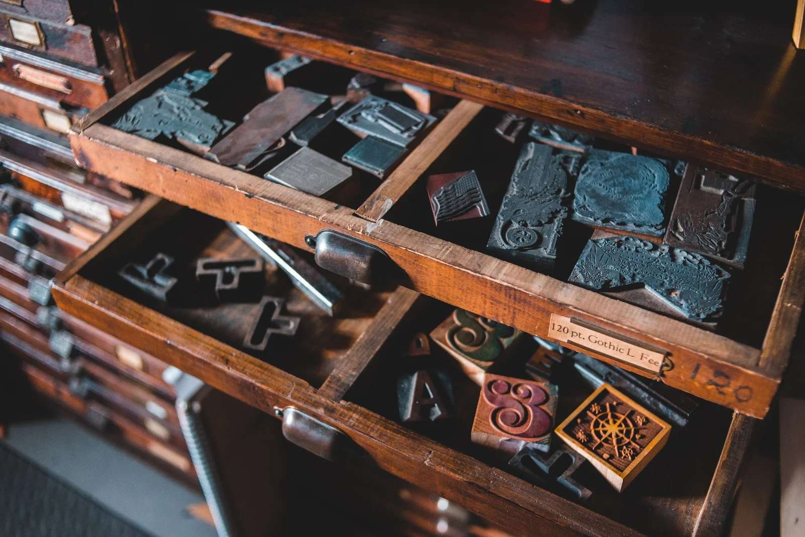 An open wooden letterpress drawer with metal and wooden printing blocks arranged in separate compartments.