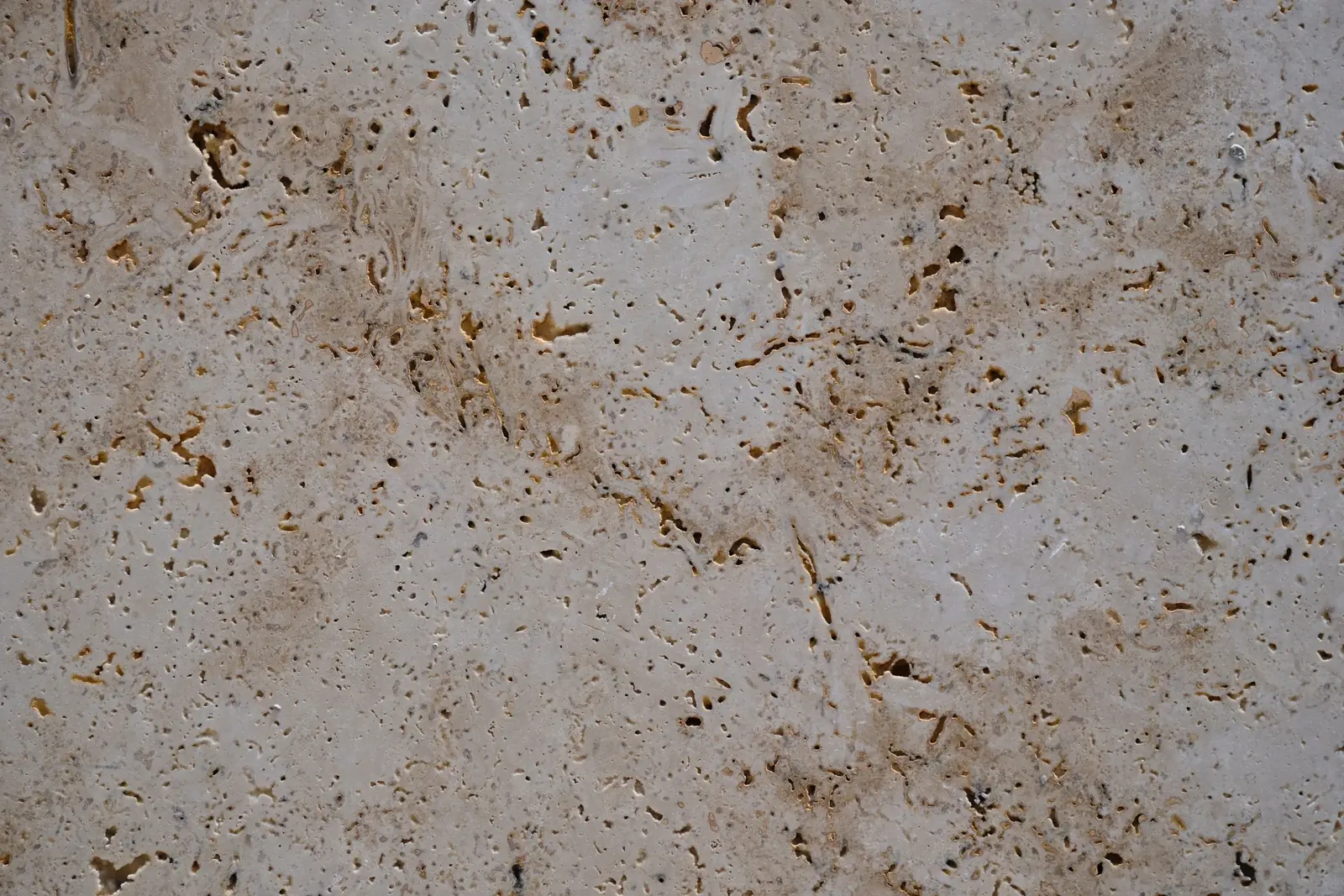 A close view of a pale beige travertine stone surface with fine pitting and faint natural veining.