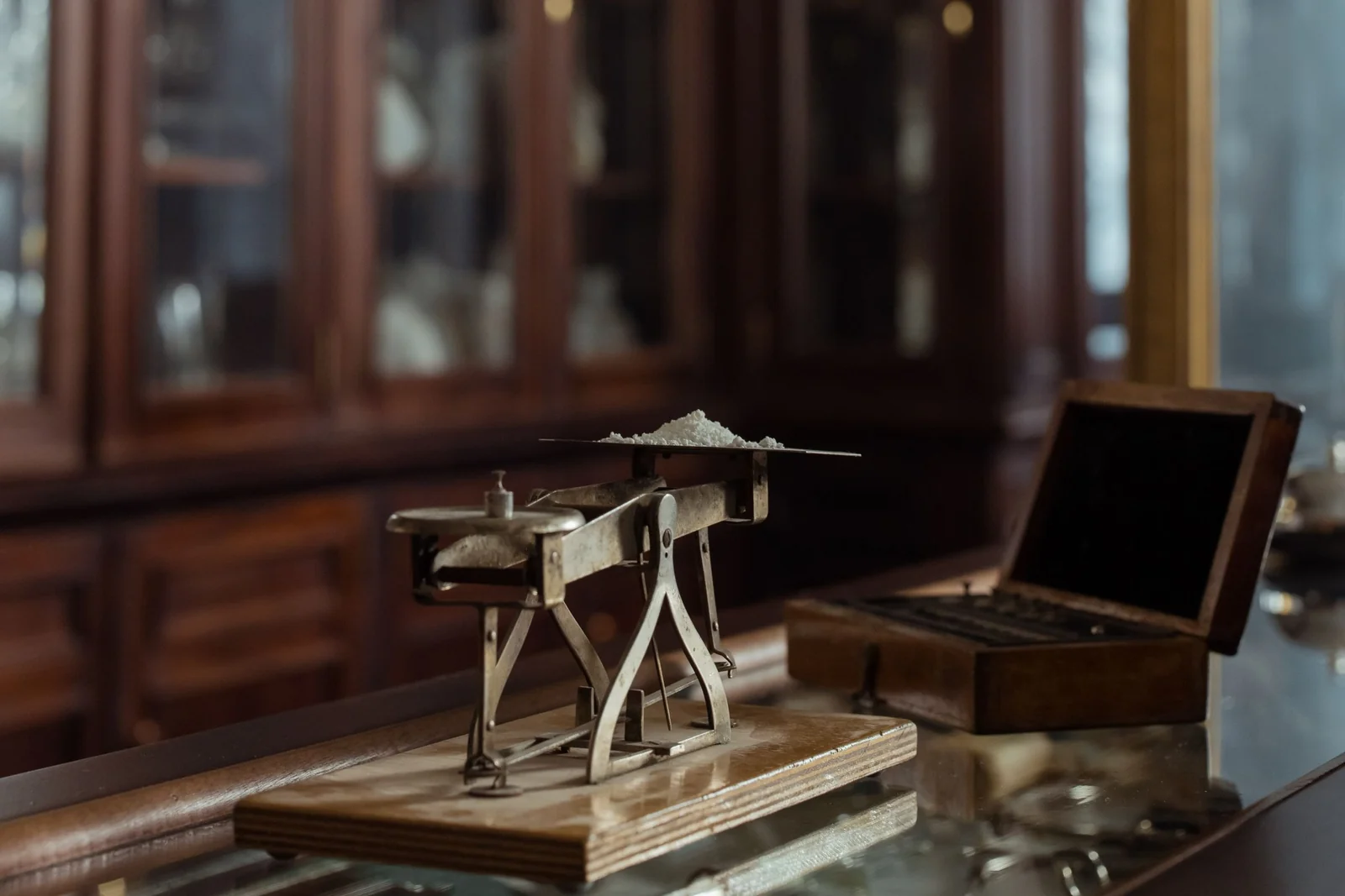 A precision balance on a counter in front of mahogany apothecary cabinets.