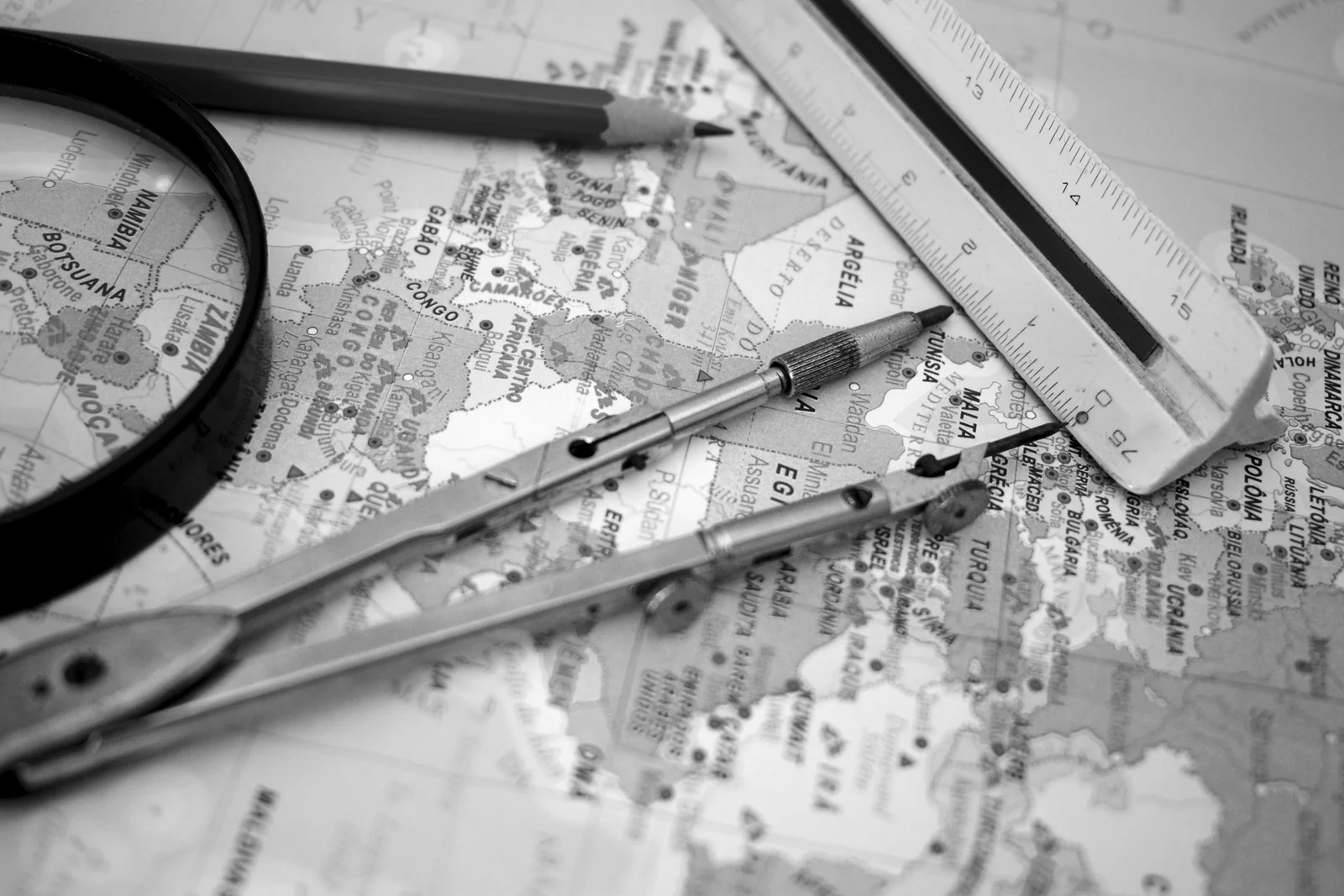A pair of drawing compasses, a steel ruler and a magnifier resting on a folded map, black and white.
