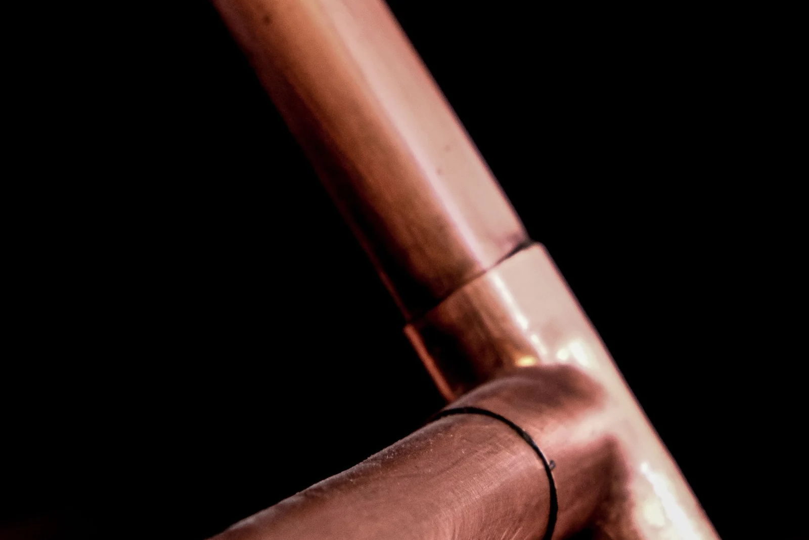 A soldered copper pipe T-junction photographed against a black background.