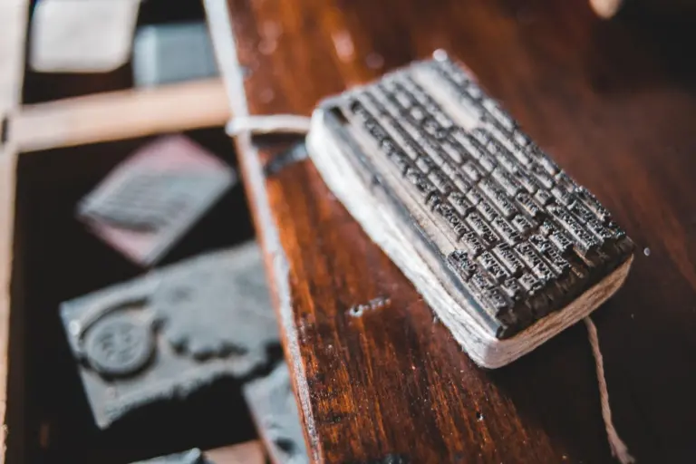 A block of metal letterpress type tied with string, resting on a dark polished wooden table.