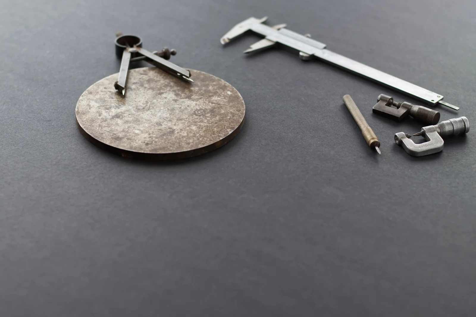 A pair of dividers and a vernier caliper laid side by side on a dark surface with small metal fittings.