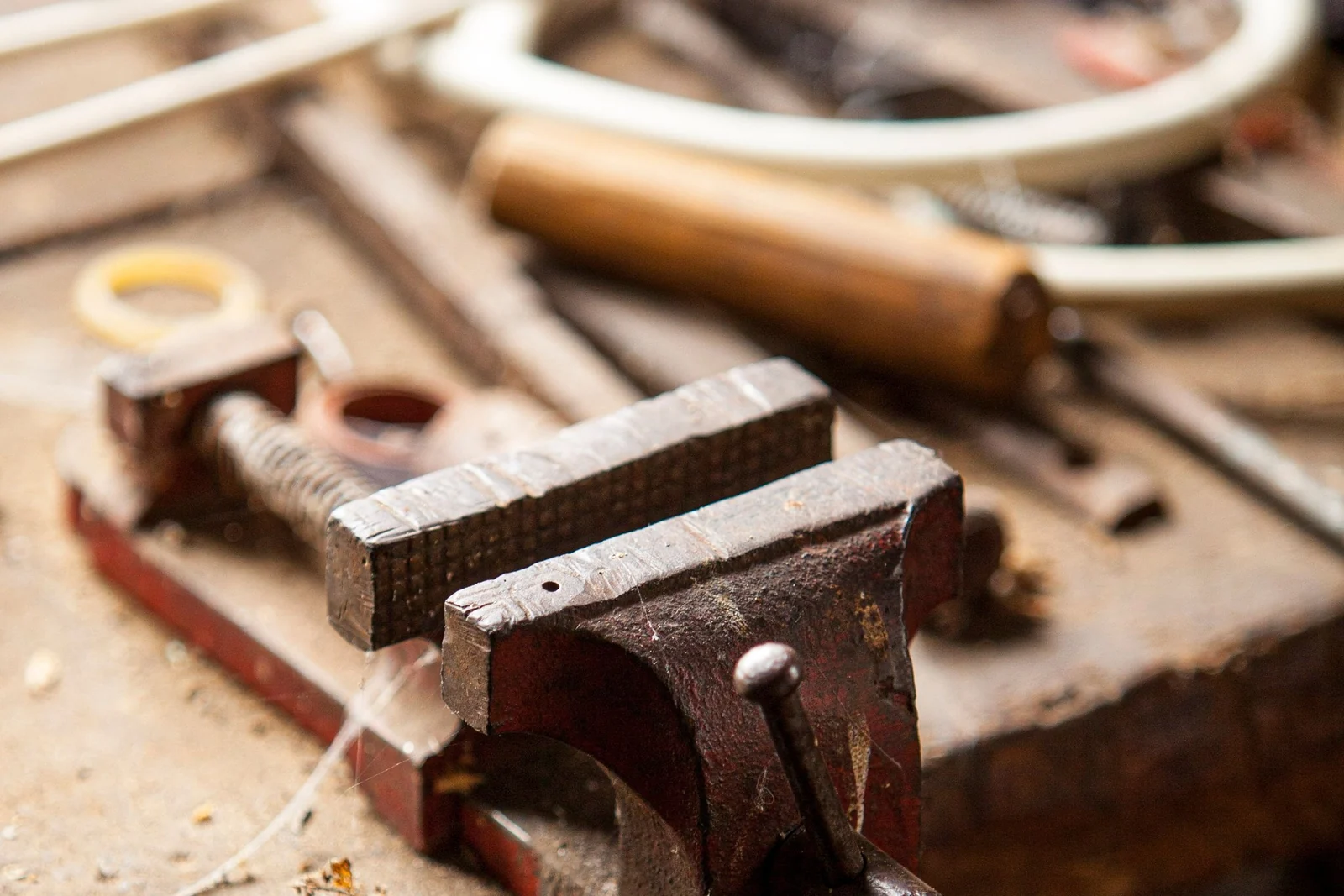 A metal bench vice mounted on a worn wooden workbench, with hand tools lying around it.