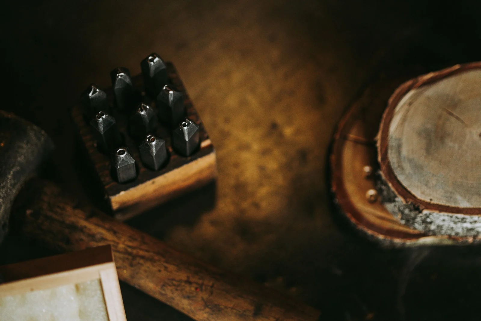 A set of steel letter punches in a wooden block on a dark workbench, beside a hammer.