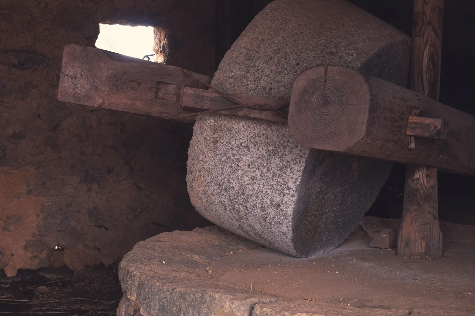 An upright stone grinding wheel resting on a circular stone base in a dim, timber-framed mill interior.