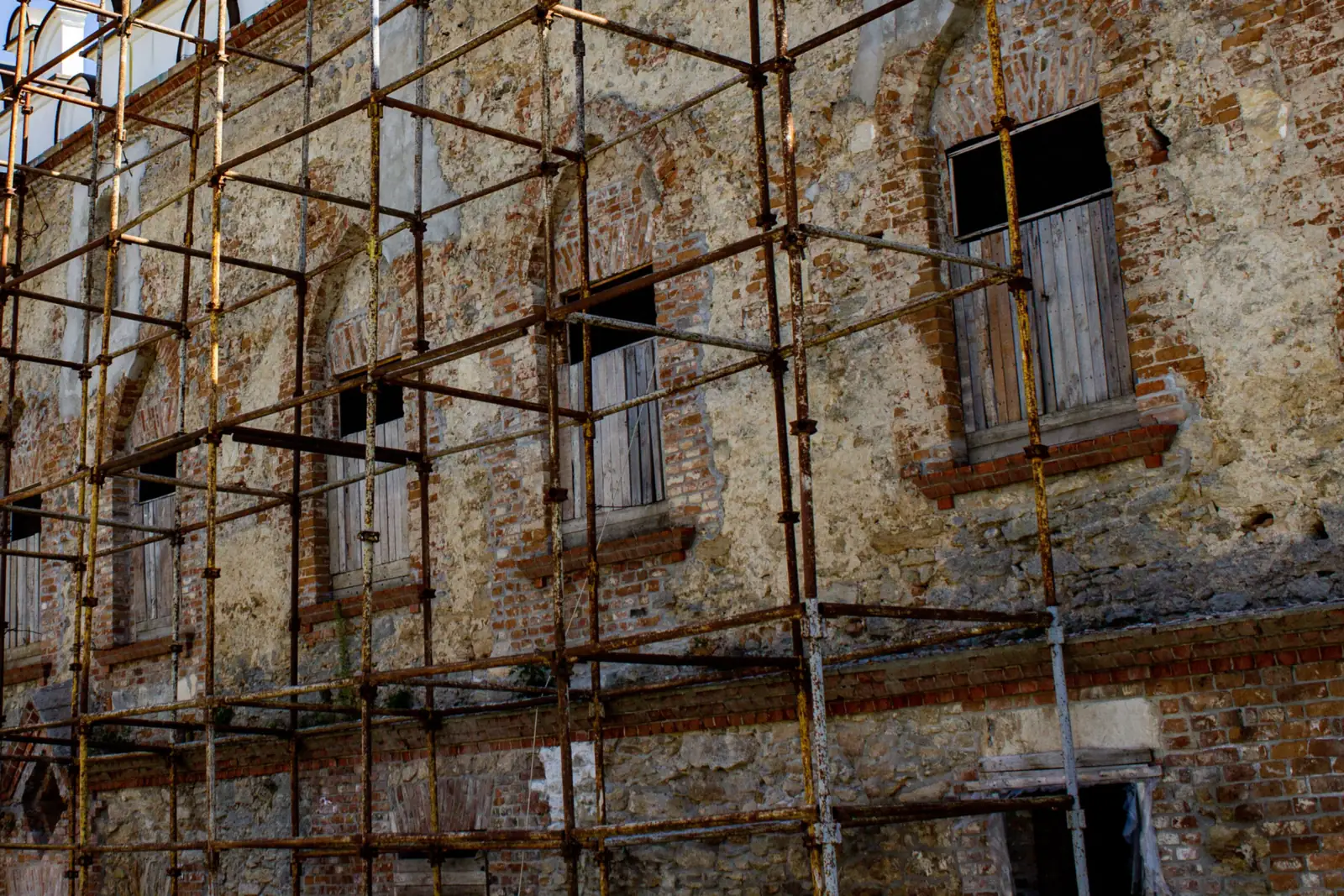 Rusted metal scaffolding standing against the weathered stone facade of an old building.