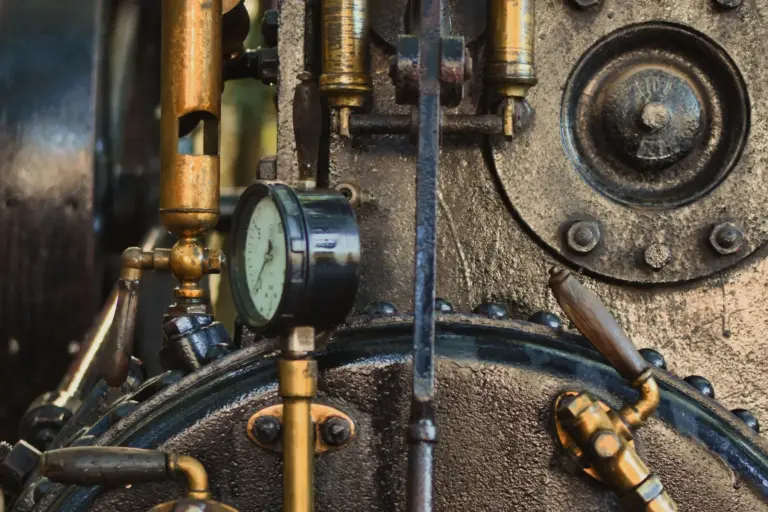 Brass pipes, a pressure gauge and valves mounted on the dark cast iron body of an old steam engine.