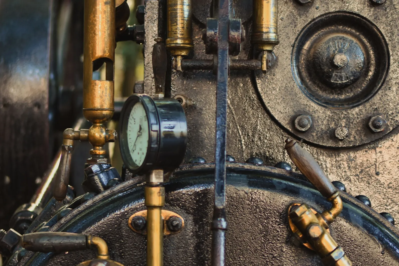Brass pipes, a pressure gauge and valves mounted on the dark cast iron body of an old steam engine.