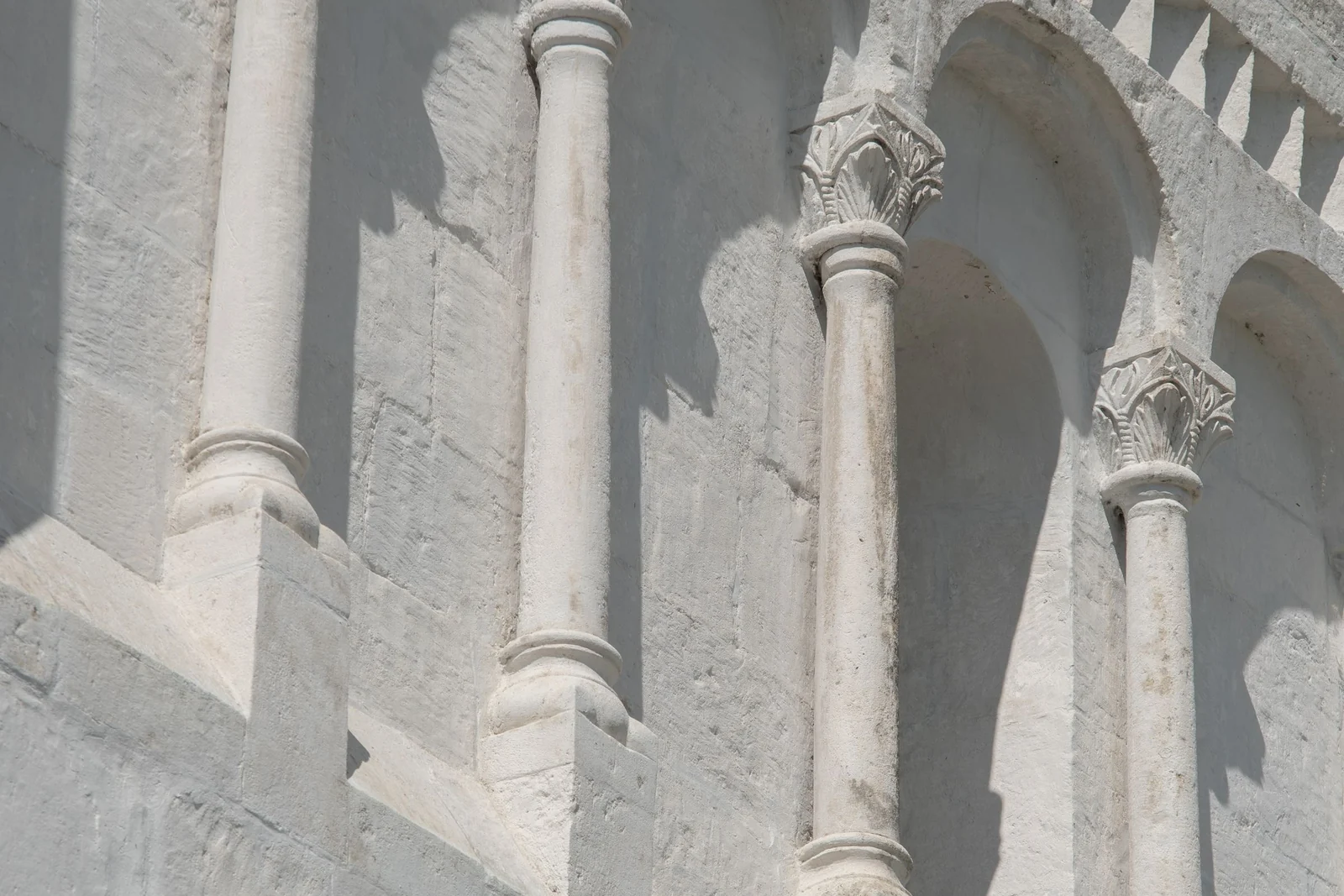 A close view of slender stone columns and carved capitals on the facade of an old building.