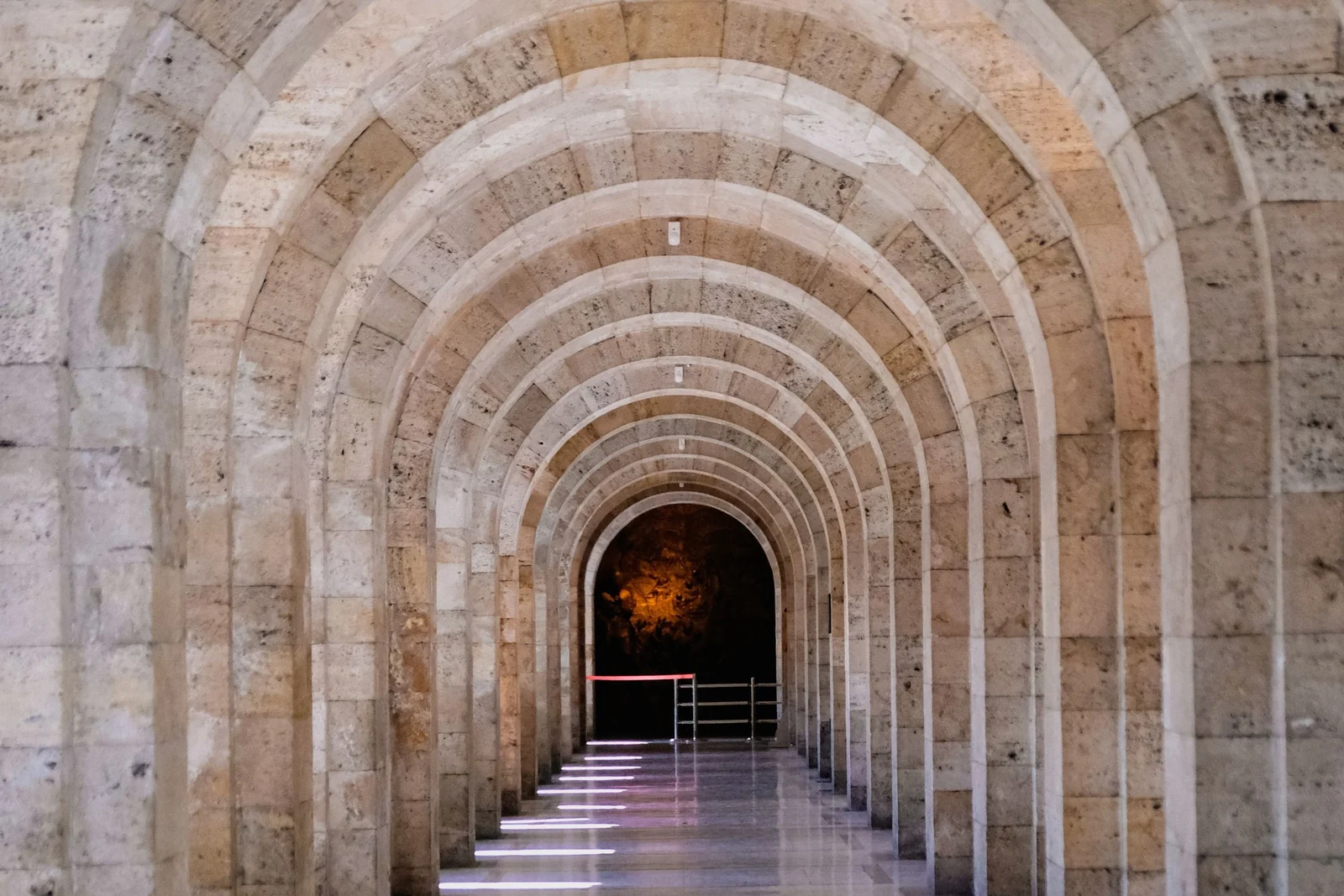 A long stone corridor of identical barrel vaults receding into the distance, with evenly spaced pools of sunlight on the floor.