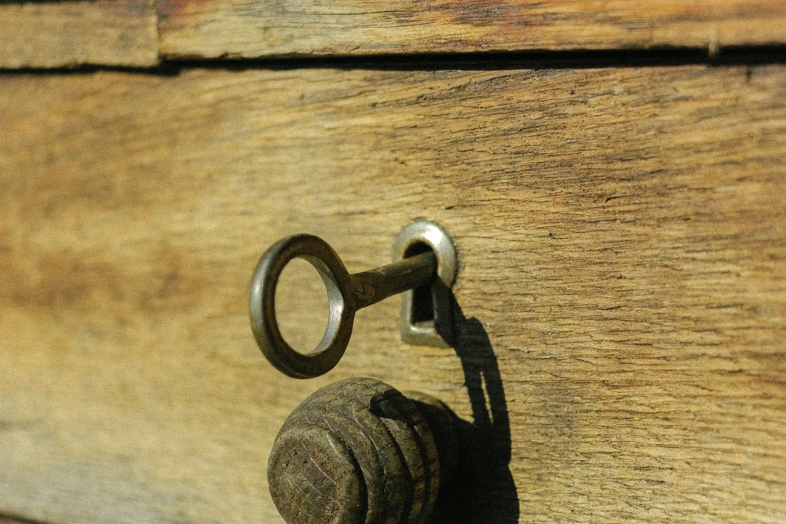 A key left in the lock plate of a weathered wooden drawer.