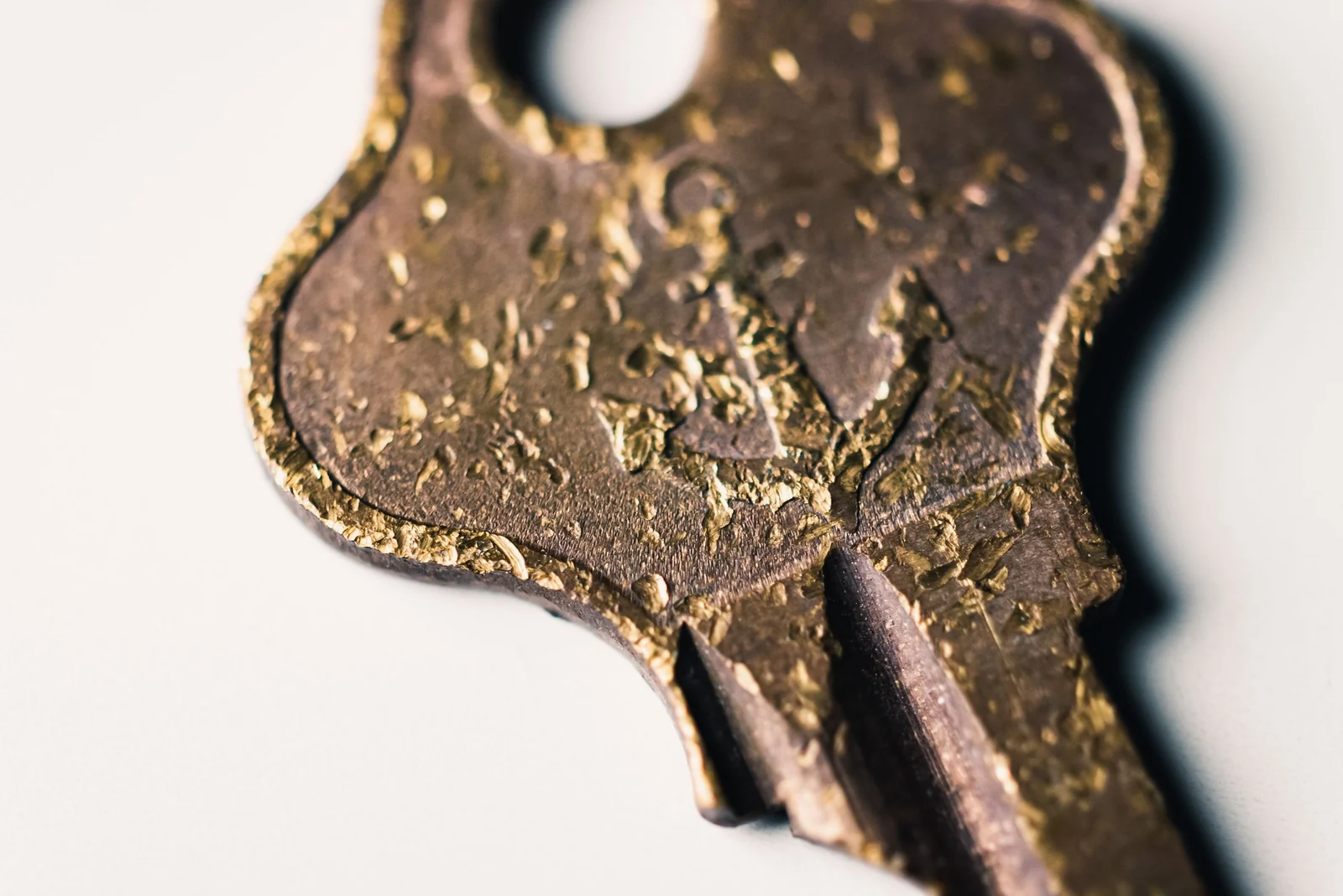 An extreme close-up of an old brass key with a worn, pitted surface lying on a pale background.