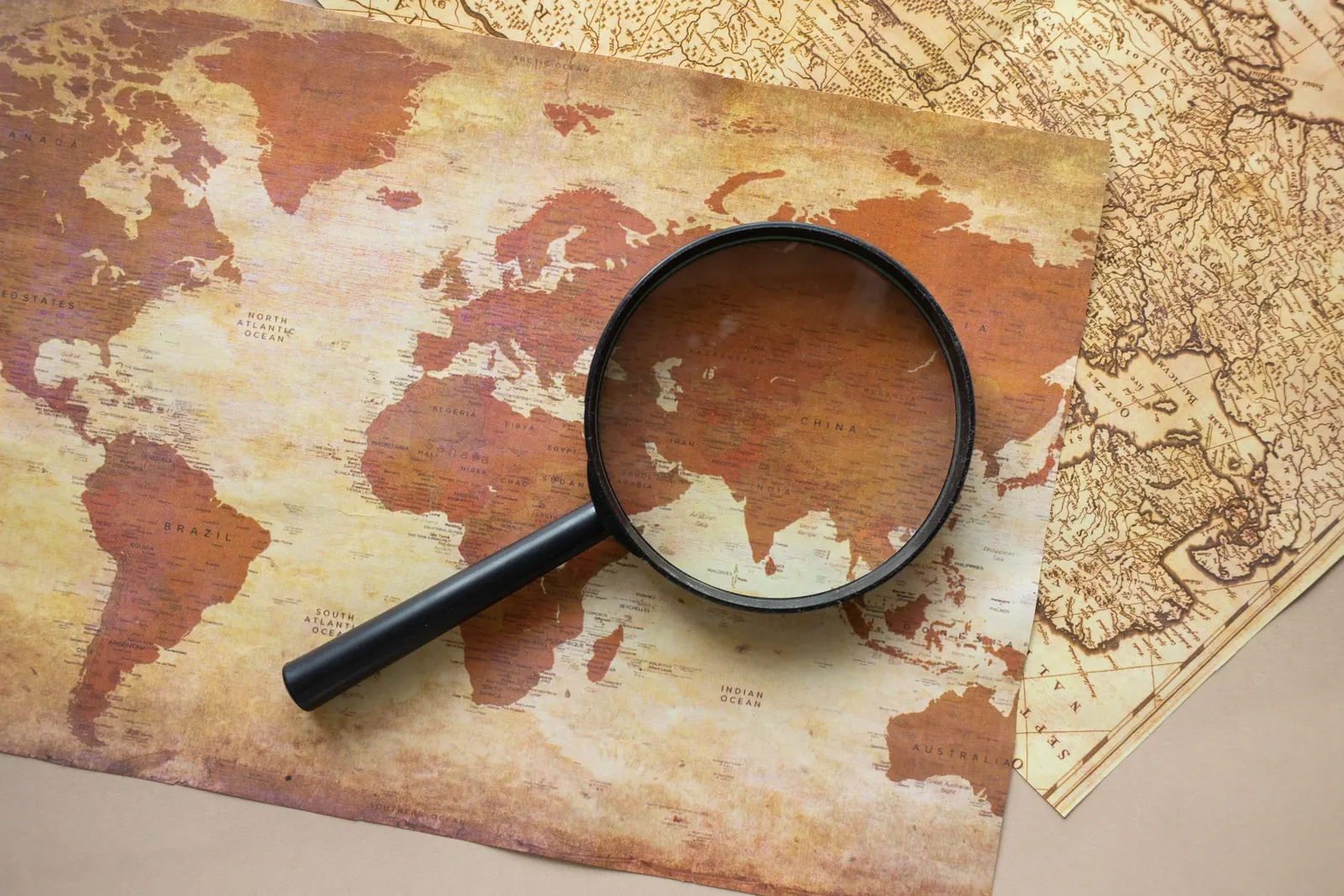 A magnifying glass resting on an old world map, enlarging one region of it.