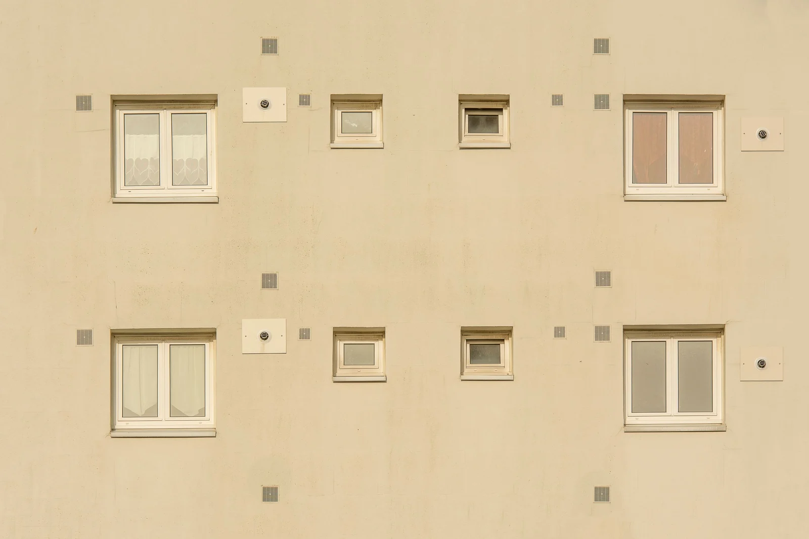 A pale facade with two rows of windows in mirrored pairs, large on the outside and small towards the centre.