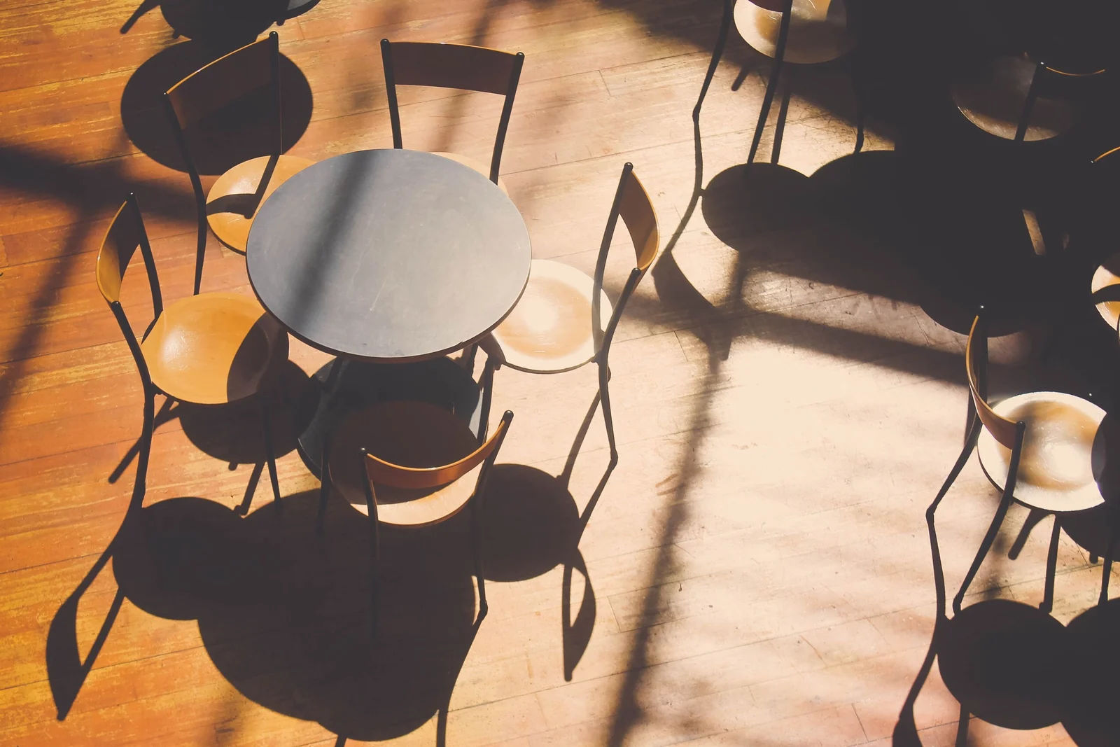Sunlight falls across an empty cafe, its round table and bentwood chairs throwing long shadows over the wooden floor.