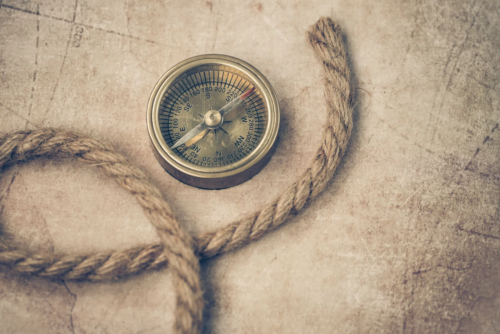 A brass pocket compass rests beside a coil of rope on a faded, weathered paper surface.