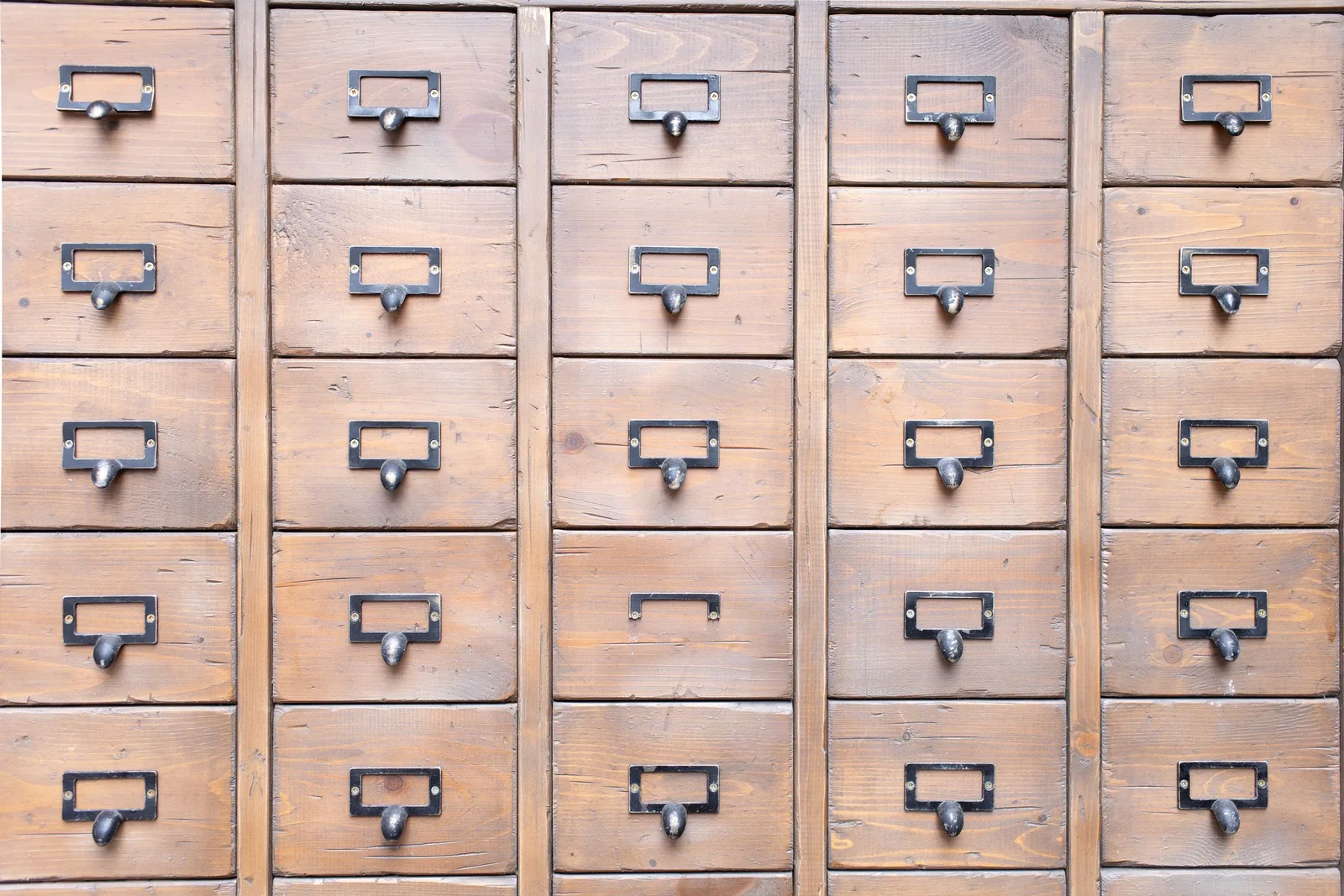 A wall of small wooden drawers, each with a metal handle and label holder, forms an even grid.
