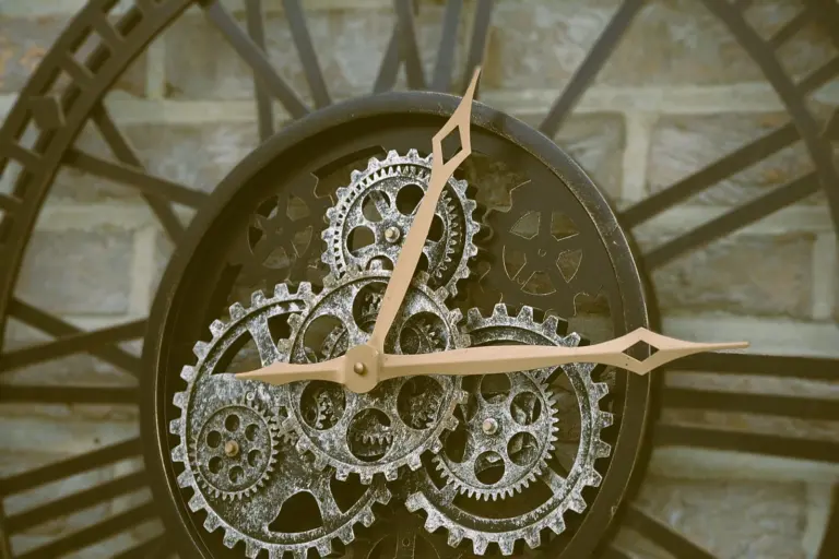 A wall clock with an open face, its hands moving over a cluster of exposed silver gears.