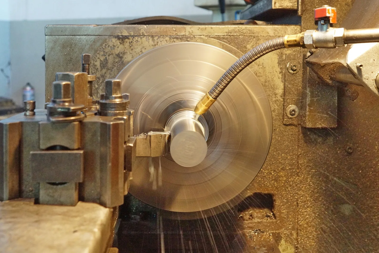 A metal lathe at work, its spinning chuck blurred and a coolant pipe bent over the workpiece.