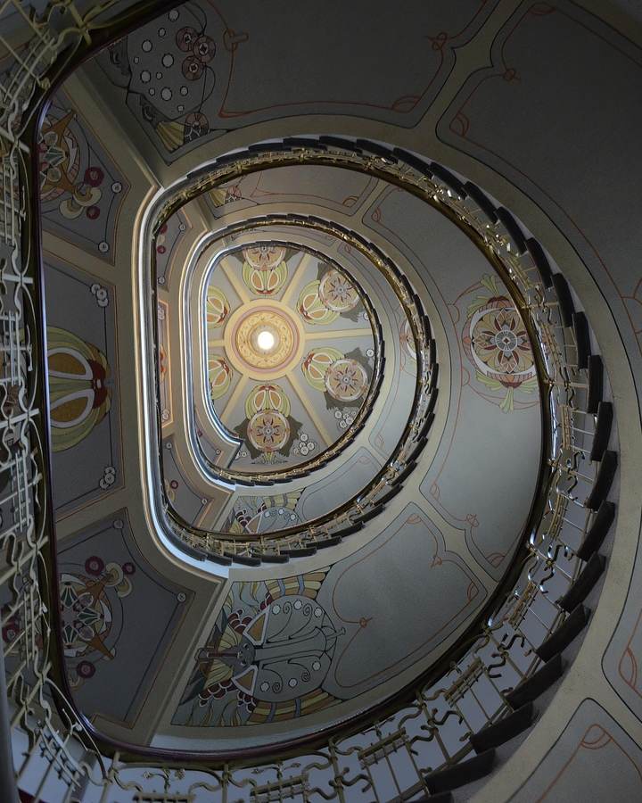 Looking up a spiral staircase towards a painted ceiling.